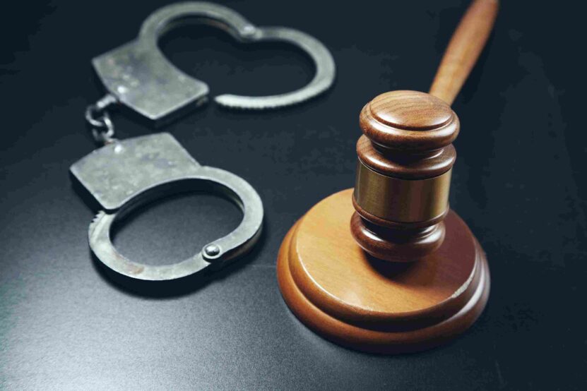 Metal handcuffs beside a wooden judge's gavel on a dark surface.