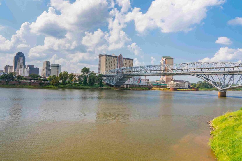 Mississippi River with a large steel bridge and city skyline under a blue sky.