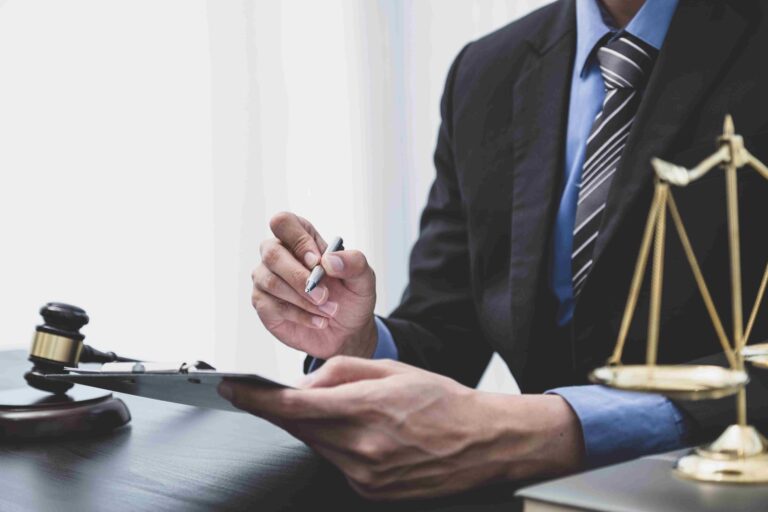 Legal professional reviewing paperwork with a pen, judge's gavel and scales of justice on the desk.